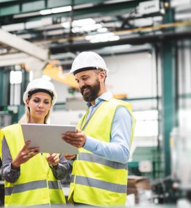 A portrait of a mature industrial man and woman engineer with tablet in a factory, talking.