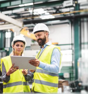 A portrait of a mature industrial man and woman engineer with tablet in a factory, talking.